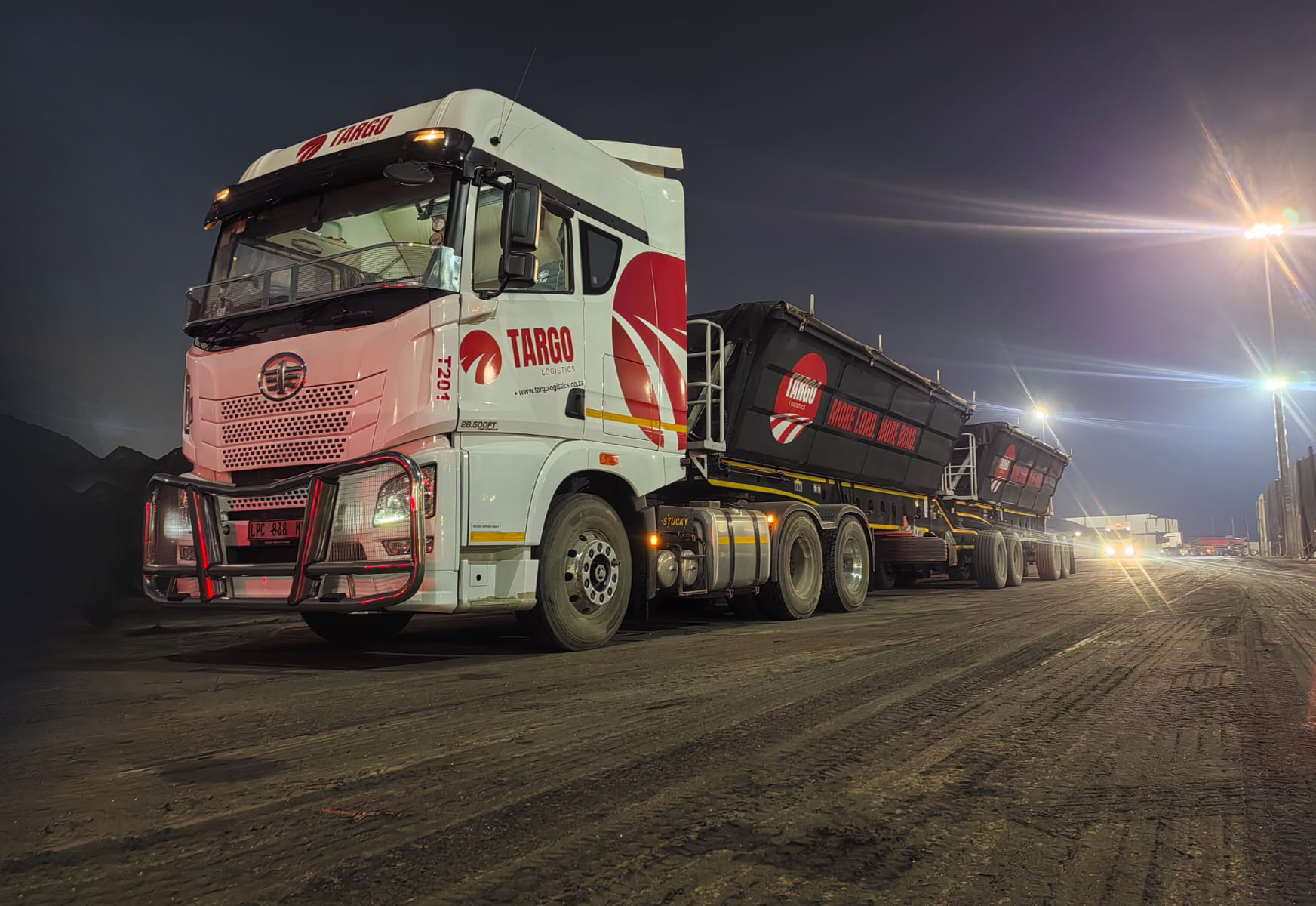 Targo Logistics FAW truck with side-tipper trailers at a bulk yard under golden yard lights